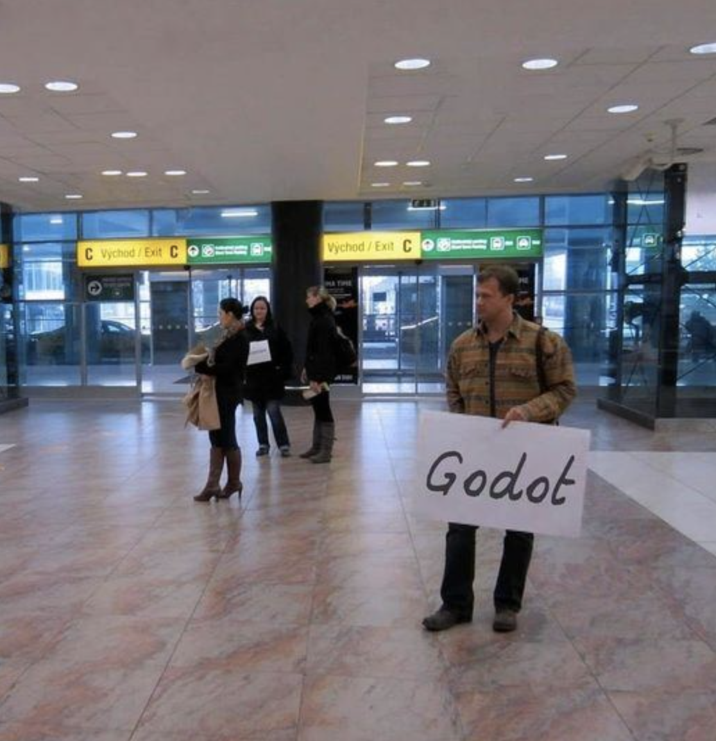 Man holding sign at an airport with the name "Godot."